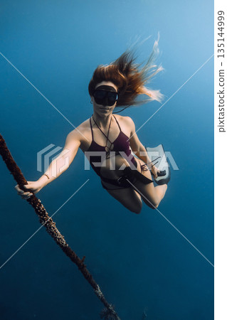 Woman freediving underwater holding rope and exploring ocean in calm blue water Woman freediving underwater holding rope and exploring ocean in calm blue water 135144999