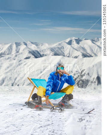 Digital poster with relaxed skier resting on deck chair in snow. 135145001