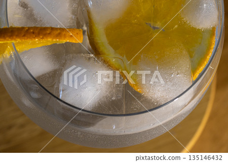 Very close up of a top view image of fresh gin tonic cocktail with ice cubes and orange slices Very close up of a top view image of fresh gin tonic cocktail with ice cubes and orange slices 135146432