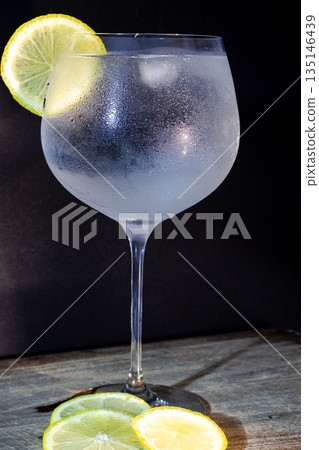 Vertical picture of fresh gin tonic cocktail with lemon slice and ice. Black background 135146439