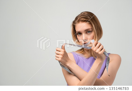 Fit young woman holding crossed measuring tape, body assessment and weight management concept, fitness goals and healthy lifestyle isolated on neutral background 135146783