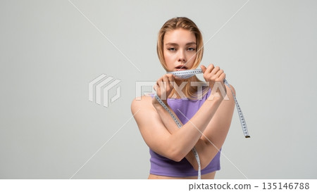Young athletic woman holding measuring tape near face, body measurement and fitness assessment concept, weight control isolated on clean studio background Young athletic woman holding measuring tape near face, body measurement and fitness assessment concept, weight control isolated on clean studio background 135146788