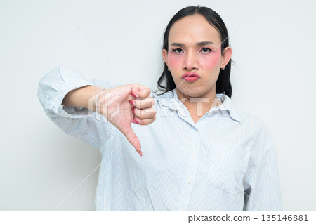 Portrait of a young Thai transgender person with thumbs down gesture against white background Portrait of a young Thai transgender person with thumbs down gesture against white background 135146881