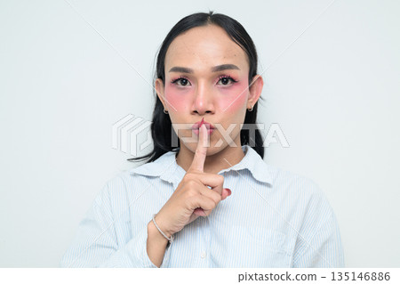 Portrait of a young Thai transgender person with finger on lips against white background Portrait of a young Thai transgender person with finger on lips against white background 135146886