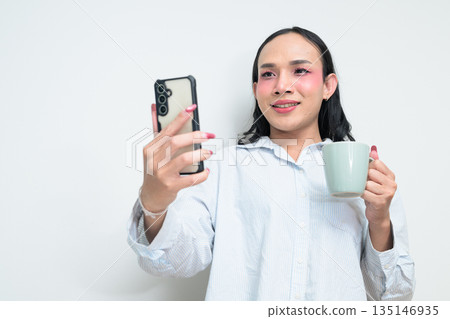 Portrait of Thai transgender person using phone and holding coffee cup against white background 135146935