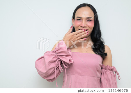 Portrait of a young Thai transgender person against white background laughing and covering mouth Portrait of a young Thai transgender person against white background laughing and covering mouth 135146976