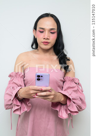 Portrait of a young Thai transgender person against white background using phone texting Portrait of a young Thai transgender person against white background using phone texting 135147010