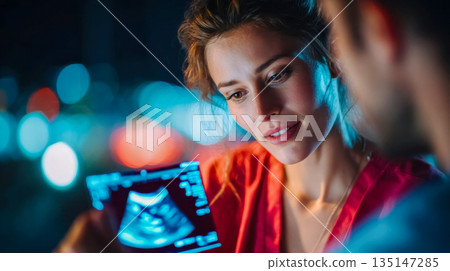Pregnant woman looking at an ultrasound image with a doctor in a softly lit medical environment 135147285