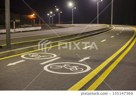 Bicycle Road Markings and Signs. Illuminated bicycle lane travel lane reserved for bicyclists with pavement markings with arrows that direct bicyclists in the direction of travel at night. Bicycle Road Markings and Signs. Illuminated bicycle lane travel lane reserved for bicyclists with pavement markings with arrows that direct bicyclists in the direction of travel at night. 135147369