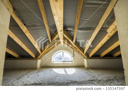 Attic of a building with wooden beams of a roof structure and a small window. 135147397