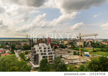 Aerial view of tower lifting crane and concrete frame of tall apartment residential building under construction in a city. Urban development and real estate growth concept. Aerial view of tower lifting crane and concrete frame of tall apartment residential building under construction in a city. Urban development and real estate growth concept. 135147438