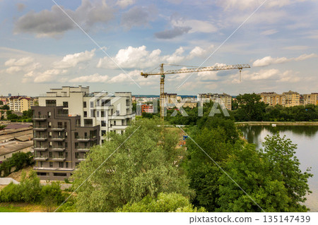 Aerial view of tower lifting crane and concrete frame of tall apartment residential building under construction in a city. Urban development and real estate growth concept. 135147439