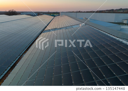 Aerial view of solar power plant with blue photovoltaic panels mounted on industrial building roof for producing green ecological electricity. Production of sustainable energy concept 135147448