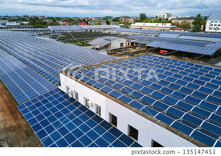 Aerial view of solar power plant with blue photovoltaic panels mounted on industrial building roof for producing green ecological electricity. Production of sustainable energy concept. Aerial view of solar power plant with blue photovoltaic panels mounted on industrial building roof for producing green ecological electricity. Production of sustainable energy concept. 135147451