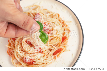 Hand adding fresh basil to spaghetti pasta with tomato sauce and parmesan cheese Hand adding fresh basil to spaghetti pasta with tomato sauce and parmesan cheese 135147531