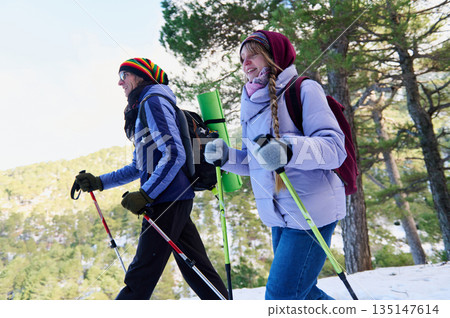 Happy Friends Hiking In Snowy Forest With Backpacks And Trekking Poles Happy Friends Hiking In Snowy Forest With Backpacks And Trekking Poles 135147614