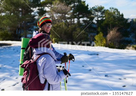 Two Friends Hiking in Snowy Field With Backpacks, Trekking Poles, and Warm Gear Two Friends Hiking in Snowy Field With Backpacks, Trekking Poles, and Warm Gear 135147627