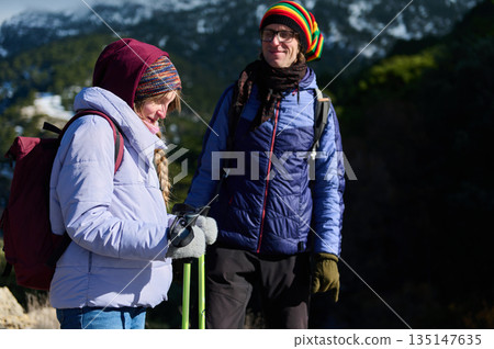 Two Friends Hiking In Winter Gear On Mountain Trail With Backpacks Two Friends Hiking In Winter Gear On Mountain Trail With Backpacks 135147635