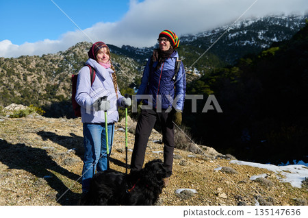 Two Women Hiking With Dog On Mountain Trail In Winter Gear 135147636