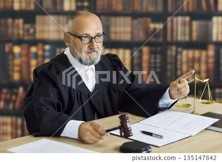 Judge pointing during courtroom hearing with scales, gavel and documents on desk Judge pointing during courtroom hearing with scales, gavel and documents on desk 135147842