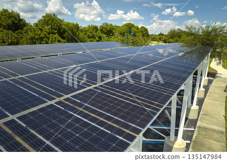 Aerial view of solar panels installed as shade roof over parking lot for parked cars for effective generation of clean electricity. Photovoltaic technology integrated in urban infrastructure Aerial view of solar panels installed as shade roof over parking lot for parked cars for effective generation of clean electricity. Photovoltaic technology integrated in urban infrastructure 135147984