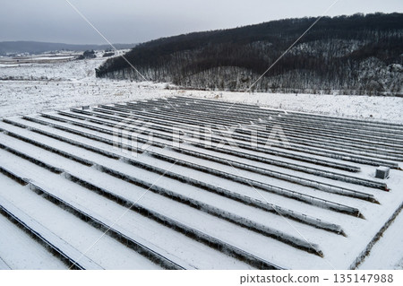 Aerial view of snow covered sustainable electric power plant with rows of solar photovoltaic panels for producing clean electrical energy. Low effectivity of renewable electricity in northern winter 135147988