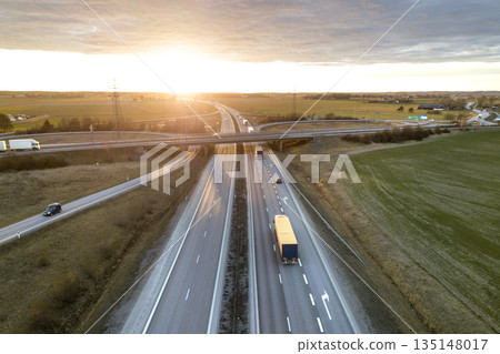 Aerial view of modern highway road intersection at dawn on rural landscape and raising sun background. Drone photography. 135148017