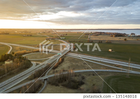 Aerial view of modern highway road intersection at dawn on raising sun background. Drone photography. Aerial view of modern highway road intersection at dawn on raising sun background. Drone photography. 135148018