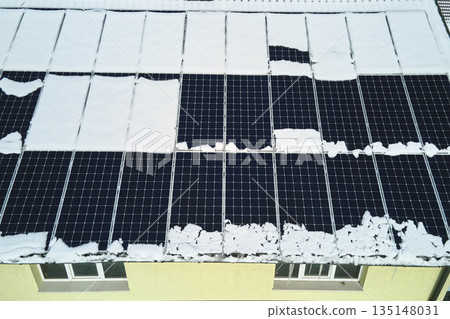 Aerial view of house roof with solar panels covered with snow melting down in winter end for producing clean energy. Concept of low effectivity of renewable electricity in northern region 135148031