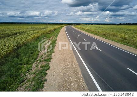 Aerial view of empty intercity road between green agricultural fields. Top view from drone of highway roadway Aerial view of empty intercity road between green agricultural fields. Top view from drone of highway roadway 135148048