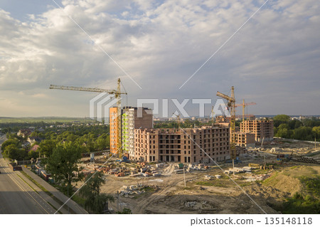 Aerial view of building site. Apartment or office building under construction. Tower cranes on suburb landscape and blue sky copy space background. 135148118