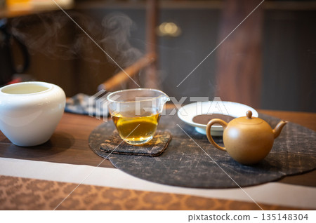 Close-Up View Of Steaming Tea With Teapot On A Circular Mat Close-Up View Of Steaming Tea With Teapot On A Circular Mat 135148304