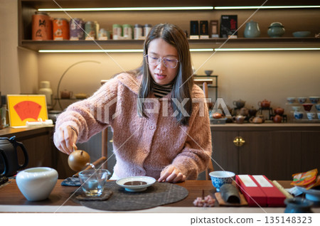 Woman Pouring Tea From A Teapot Into A Teacup At A Table Woman Pouring Tea From A Teapot Into A Teacup At A Table 135148323