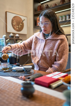 Female Tea Master Pouring Tea From A Teapot Into A Teacup At A Table Female Tea Master Pouring Tea From A Teapot Into A Teacup At A Table 135148329