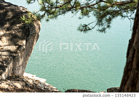 View of the blue turquoise river or lake with branches of coniferous trees and rocky shores, beautiful landscape with bright water copy space nature, tourism View of the blue turquoise river or lake with branches of coniferous trees and rocky shores, beautiful landscape with bright water copy space nature, tourism 135148423