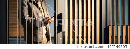 A modern metal and wood gate stands at the entrance of a contemporary house. A person is seen interacting with the gate, highlighting its stylish design at sunset, banner 135149805