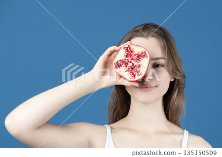 Young woman holding pomegranate half covering eye 135150509