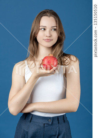 Young woman holding fresh pomegranate on a blue background Young woman holding fresh pomegranate on a blue background 135150510