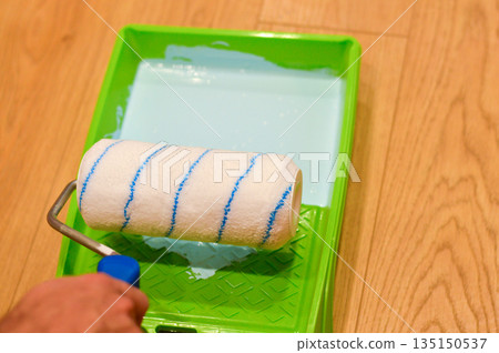 The cylindrical roller absorbs rich blue color from the plastic tray, getting loaded with paint and poised to glide smoothly across the interior surface for a new look. 135150537