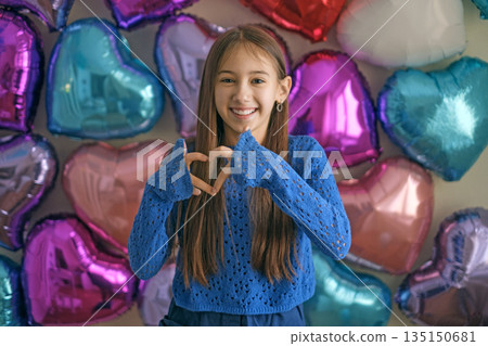 A teenage girl folded her fingers in the shape of a heart, showing a gesture of love on Valentine's day 135150681
