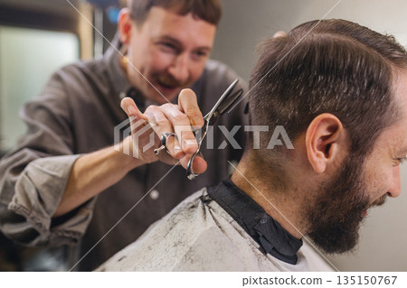 Barber cutting male client hair with scissors and comb. Close up of professional haircut process, precision technique, men grooming service in modern barbershop. Barber cutting male client hair with scissors and comb. Close up of professional haircut process, precision technique, men grooming service in modern barbershop. 135150767