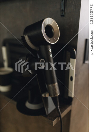 Professional hair dryer hanging on wall in barbershop. Modern grooming equipment, barber salon interior detail, hairstyling tool, clean minimal workplace concept. Professional hair dryer hanging on wall in barbershop. Modern grooming equipment, barber salon interior detail, hairstyling tool, clean minimal workplace concept. 135150778