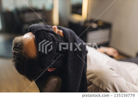 Relaxed male client lying in barber chair during classic shaving procedure. Professional barbershop service, beard grooming, comfort and men self care lifestyle concept. 135150779