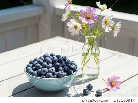 Summer still life with a bowl of fresh blueberries and cosmos flowers in a vase on a table Summer still life with a bowl of fresh blueberries and cosmos flowers in a vase on a table 135150817
