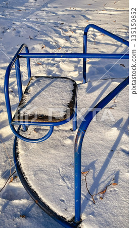 Blue metal playground carousel covered in fresh white snow on a bright sunny winter day in the park Blue metal playground carousel covered in fresh white snow on a bright sunny winter day in the park 135150852