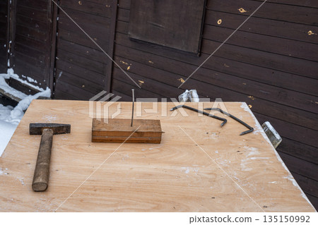 Hammer, nail and metal hooks arranged on a wooden workbench outdoors in winter. Construction and repair concept in cold snowy conditions. Hammer, nail and metal hooks arranged on a wooden workbench outdoors in winter. Construction and repair concept in cold snowy conditions. 135150992