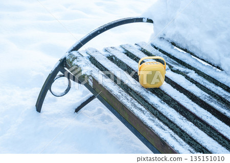 Compact yellow wireless speaker on snowy bench outdoors. Portable audio technology concept for winter travel, outdoor entertainment and modern digital lifestyle. Clean minimal background suitable for 135151010
