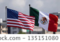 usa and mexican flags waving against a city industrial landscape and a gray cloudy sky 135151080
