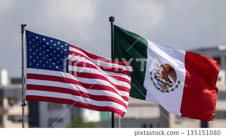 usa and mexican flags waving against a city industrial landscape and a gray cloudy sky 135151080