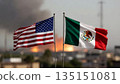 flags of the usa and mexico in the foreground against a heavy fire and thick black smoke in the city 135151081